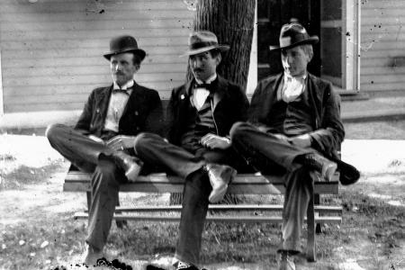 Three men sitting on a bench in front of the Worthington Presbyterian Church ca 1880-1900)